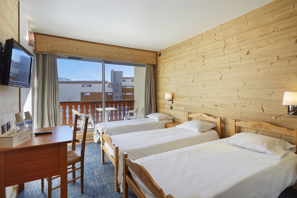 A hotel room with two beds, a desk, a chair, a TV, and a balcony with a view of buildings.