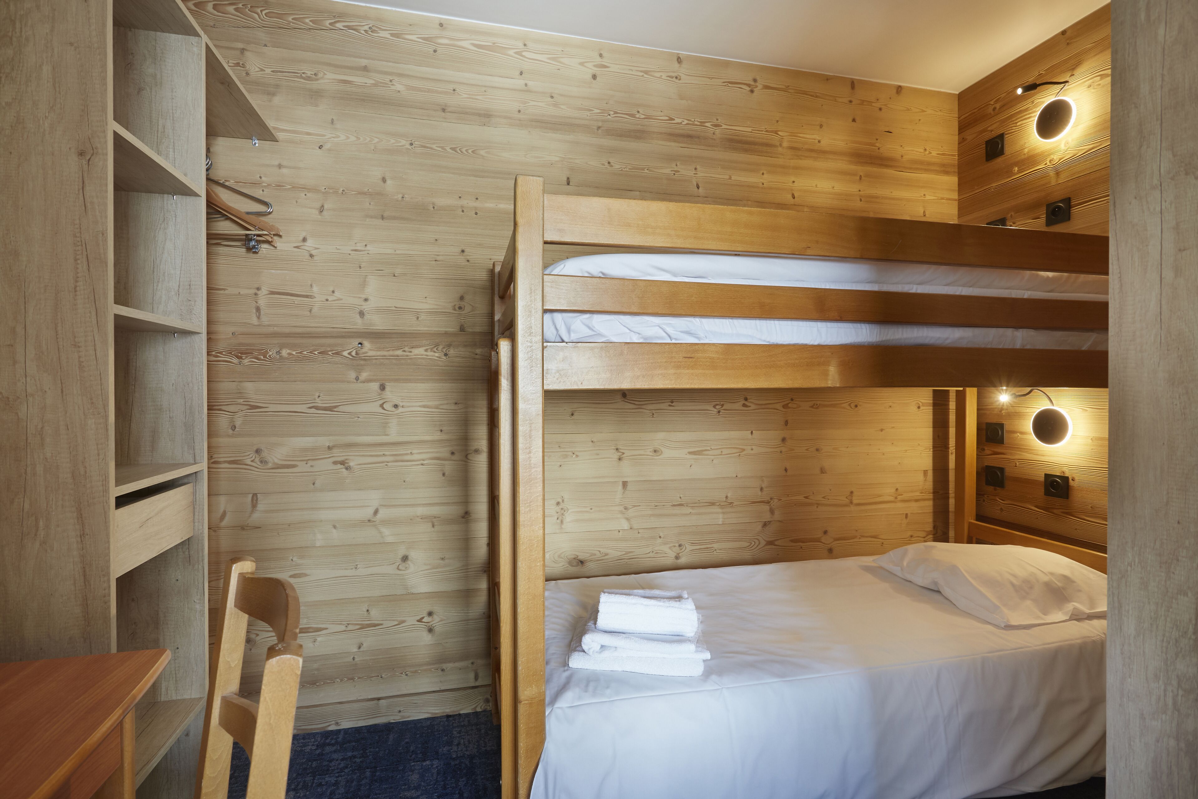 Een stapelbed met een houten hoofdbord en een bureau met een stoel.