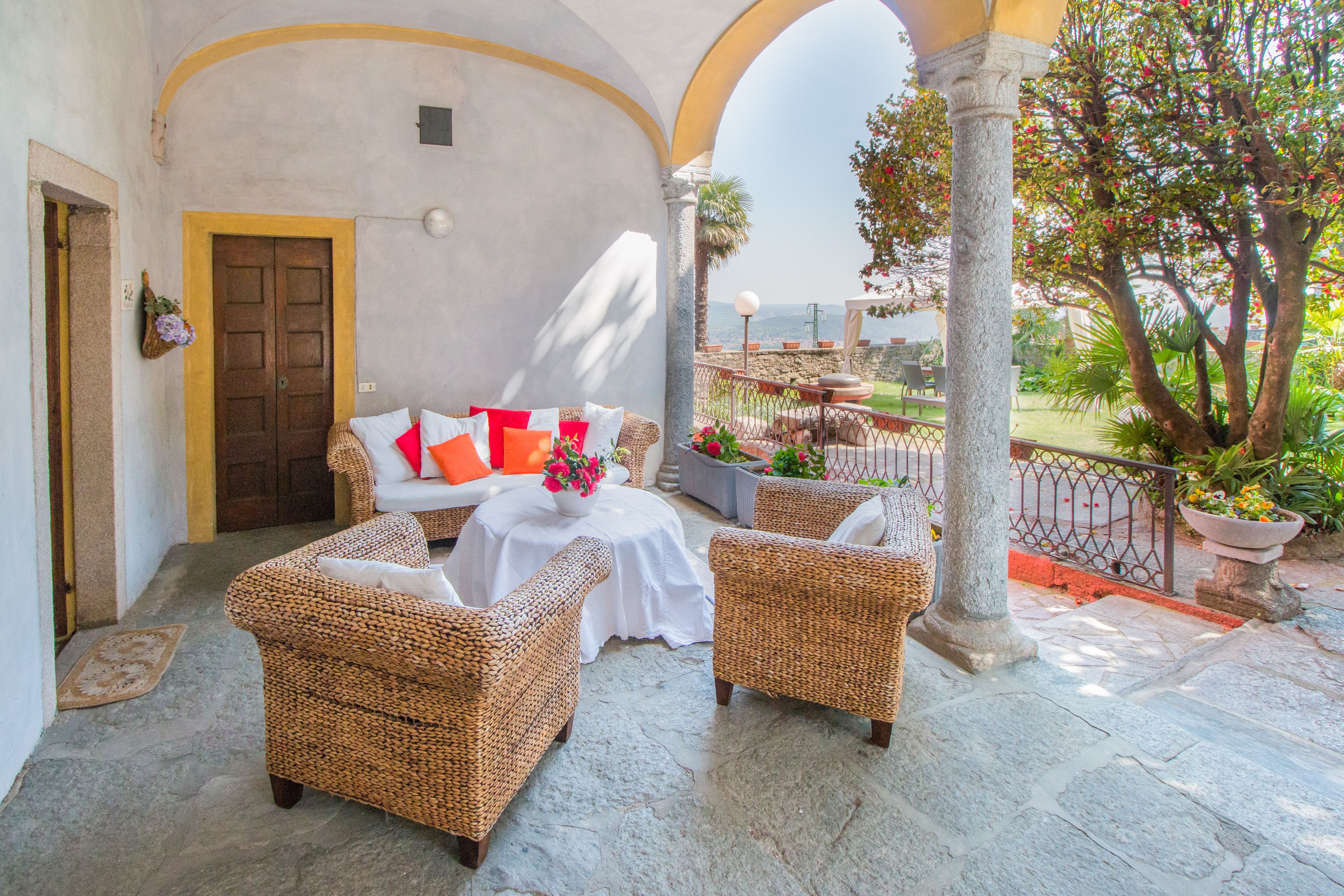 A cozy outdoor seating area with wicker furniture, a table with a vase of flowers, and a view of the landscape.