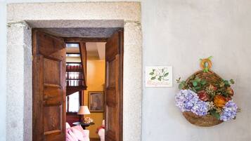 Una porta d'ingresso che dà su una stanza con un letto e una lampada, un cartello appeso al muro e un cesto di vimini con fiori.