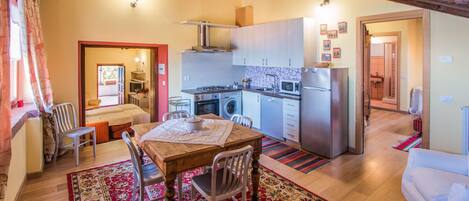 A compact kitchen with modern appliances, a dining area with a wooden table and chairs, and a living area with a sofa.