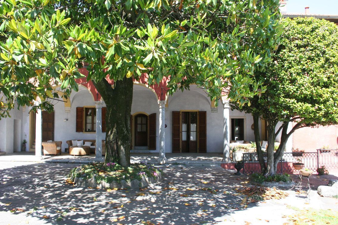 A courtyard with a large tree, a covered seating area, and a building with arched windows and doors.