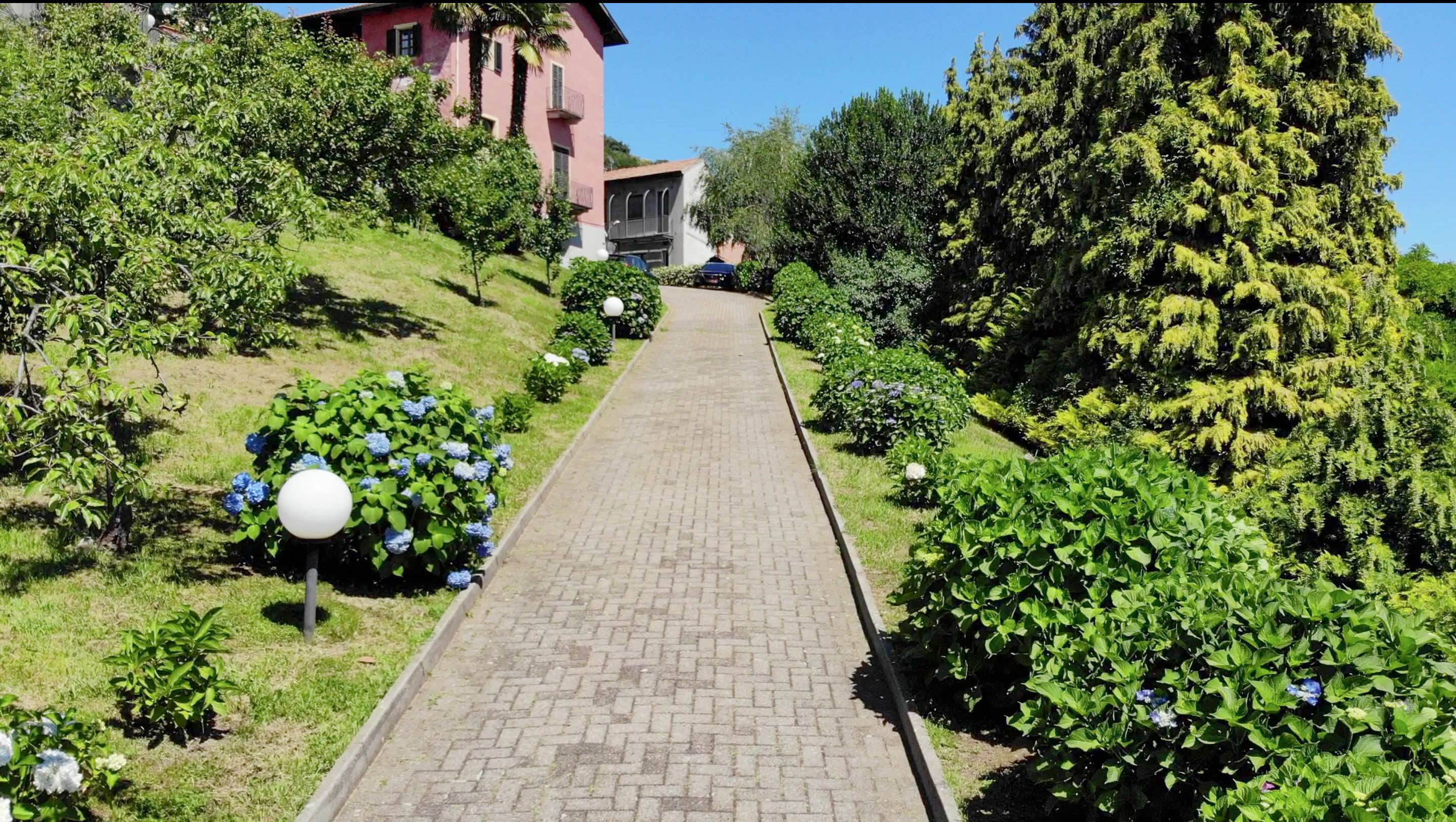 Un camí pavimentat flanquejat per vegetació exuberant i un edifici rosa amb balcons.
