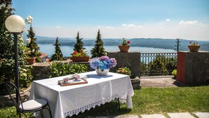 Une table d’extérieur recouverte d’une nappe blanche, un vase rempli de fleurs et une vue sur un lac et des montagnes.