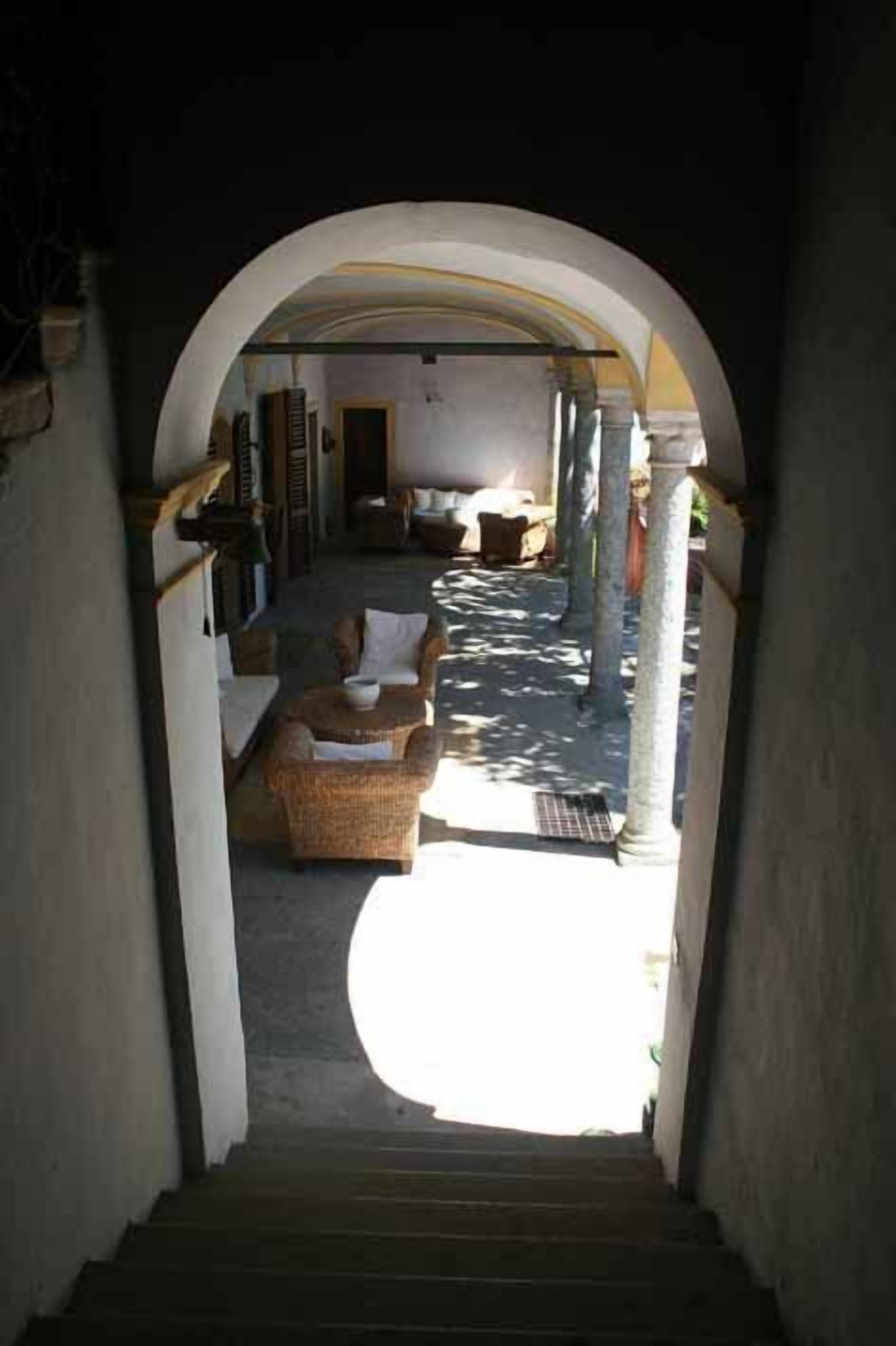 A staircase leading to a sunlit outdoor area with wicker furniture and a stone column.