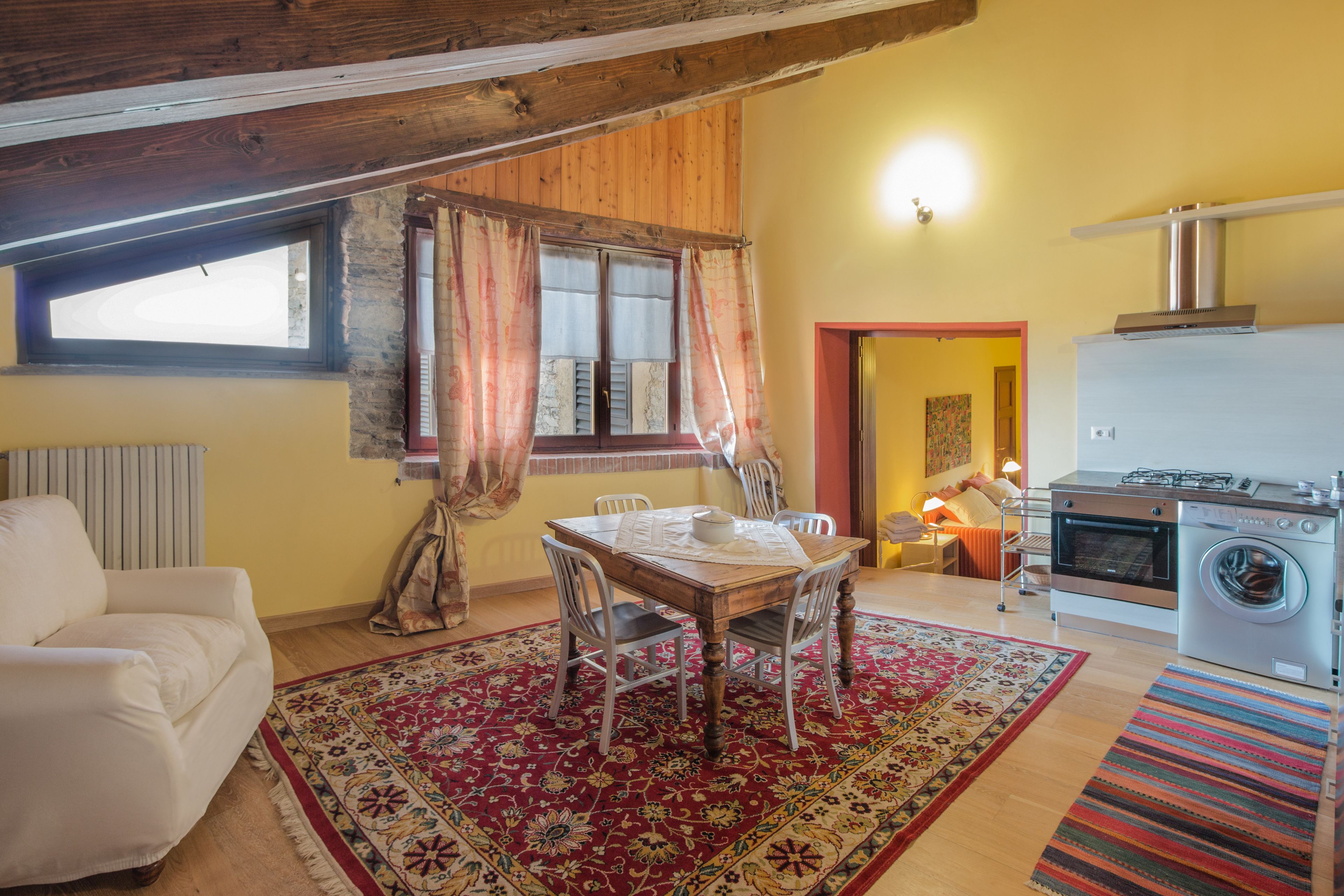 Ein gemütliches Wohnzimmer mit einem Holztisch, Stühlen, einer Couch und einem roten Teppich mit Muster.