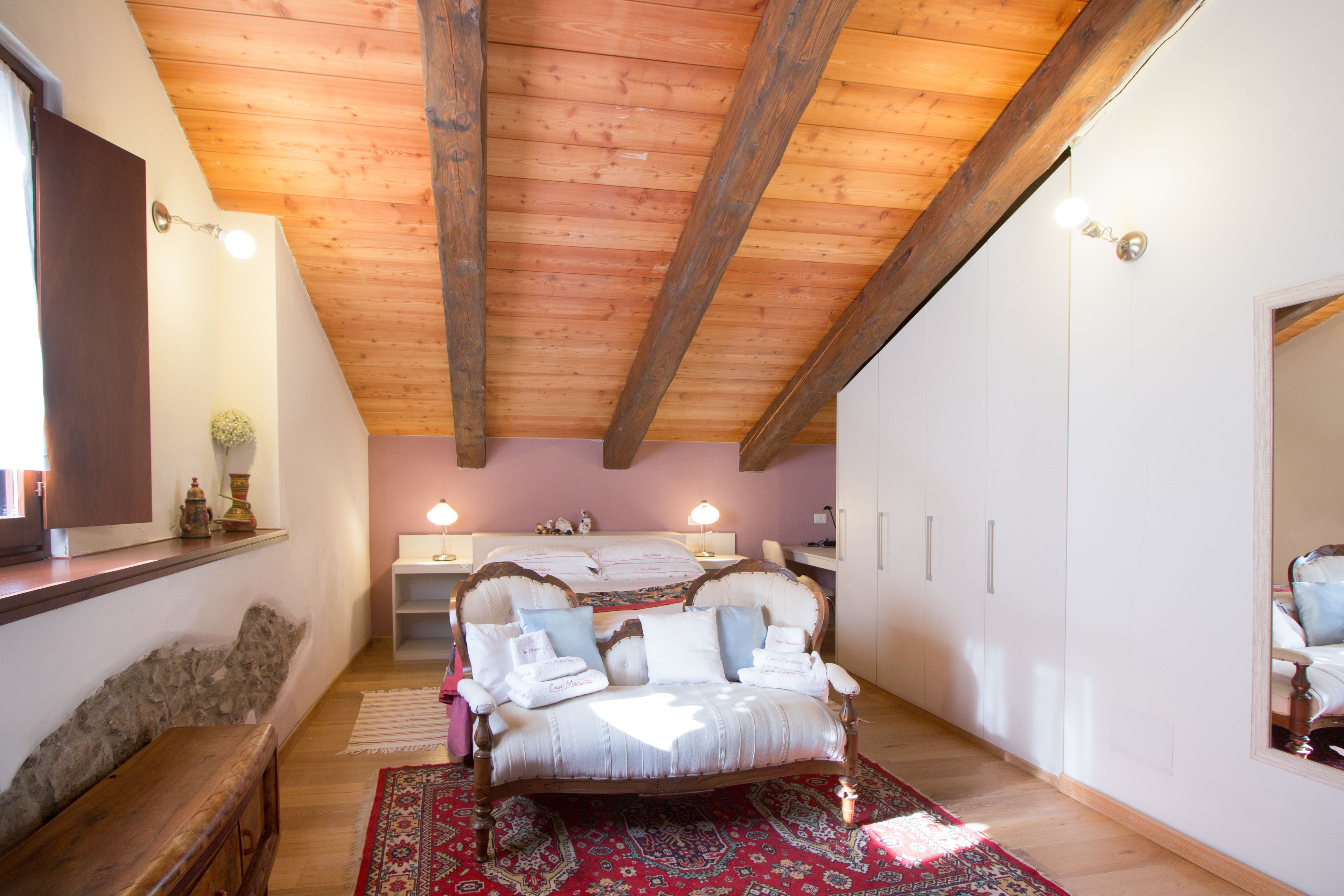 Ein Schlafzimmer mit Holzboden, einem Bett mit weißen Leinen, einem roten Teppich mit Muster und einer Steinsäule.