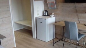 A compact kitchenette with a white refrigerator, a small table, and a grey chair. - Pan Garden Åmli Hotel (Amli)