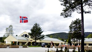 A building with a flag, outdoor seating, and a mountainous backdrop. - Pan Garden Åmli Hotel (Amli)