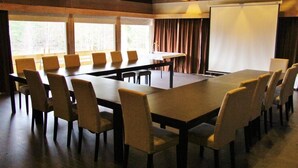 A conference room with a large table and chairs, a projector screen, and windows with curtains. - Pan Garden Åmli Hotel (Amli)