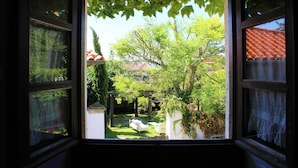 Vista a través de una ventana que muestra un jardín con una pérgola, un banco blanco y un árbol.