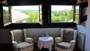 Habitación con dos sillones mirando una mesa con una botella y vasos, y vista a un tejado con tejas y follaje afuera.