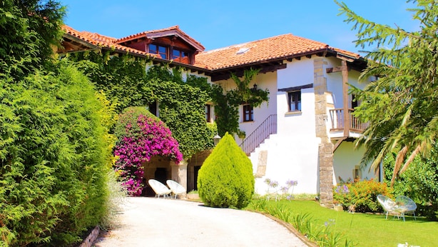 Una villa con tejado de baldosas, fachada de piedra y un jardín bien cuidado con un camino que lleva a la entrada.