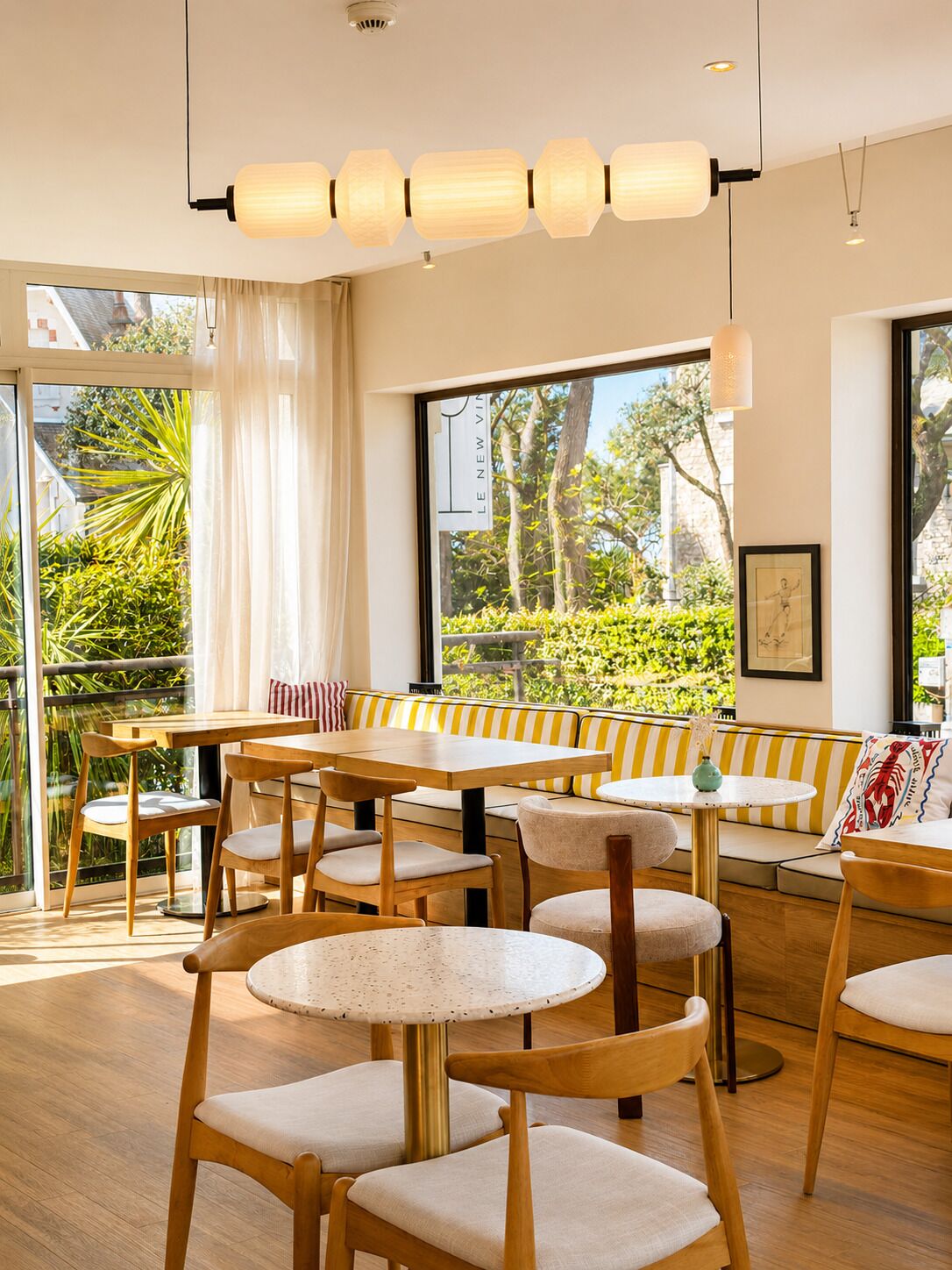 A modern dining area with wooden furniture, large windows, and a view of greenery.