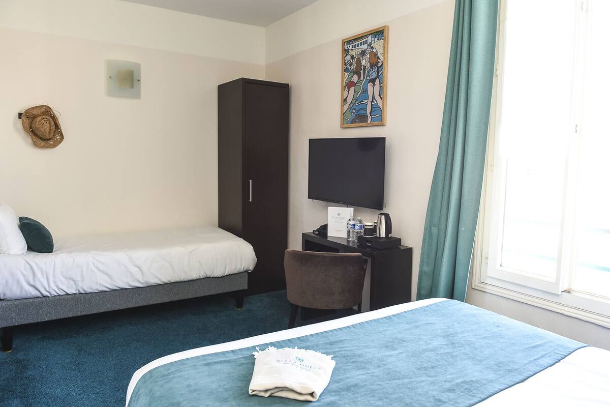 Une chambre d’hôtel avec un lit, un bureau avec une télévision, une armoire et une fenêtre avec des rideaux.