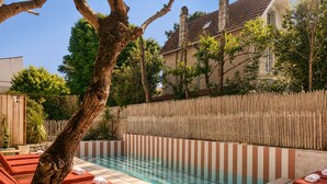 Un espace piscine avec des chaises longues, une clôture en bois et un bâtiment en arrière-plan.