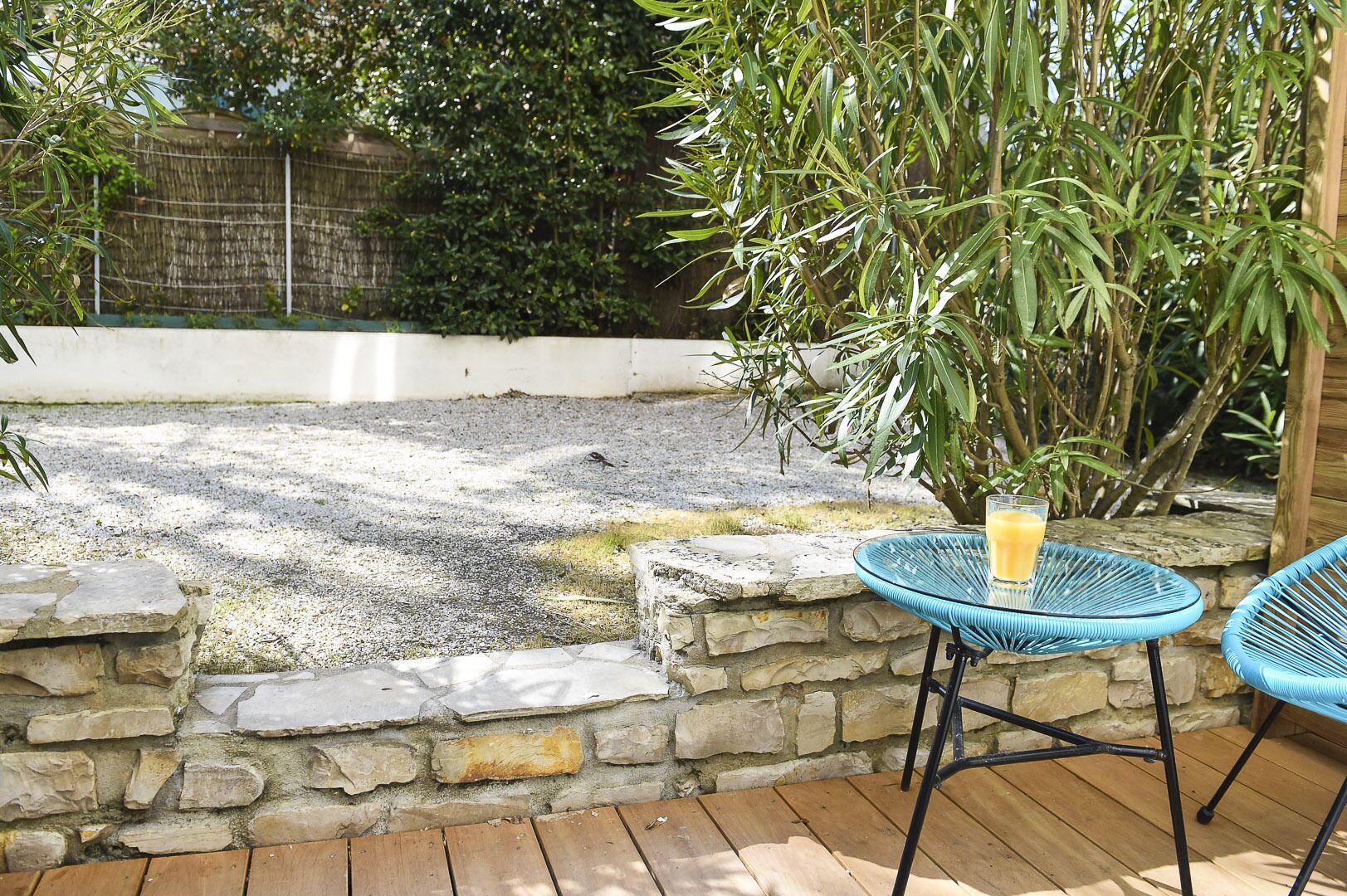 Une terrasse avec un mur en pierre, une petite piscine et une table sur laquelle se trouve un verre de jus d’orange.
