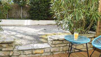 Une terrasse avec un mur en pierre, une petite piscine et une table sur laquelle se trouve un verre de jus d’orange.