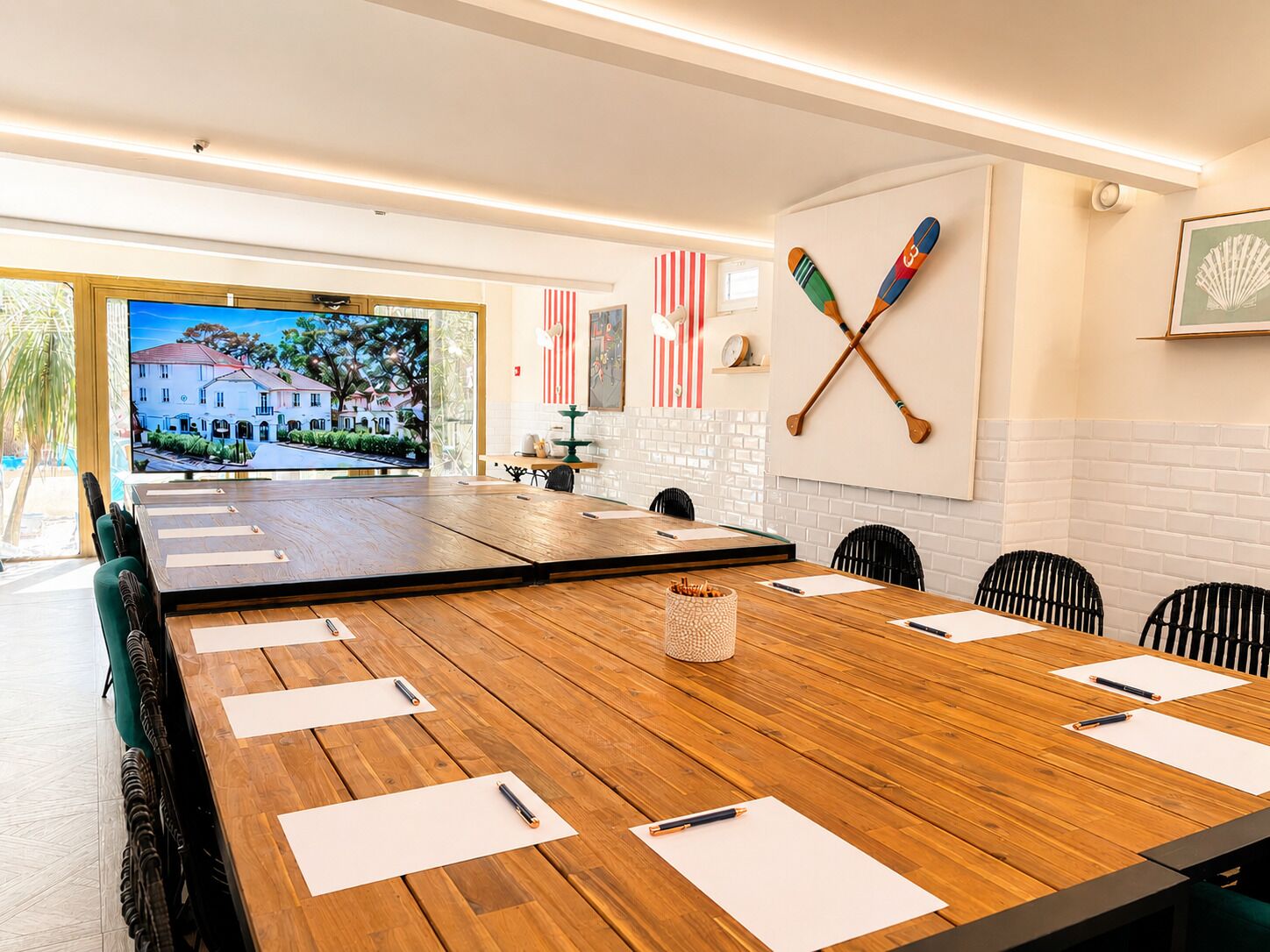 Una sala de conferències amb un gran taulell de fusta, cadires, una televisió que mostra un paisatge idíl·lic i una paret amb dues pales creuades i una bandera dels Estats Units.
