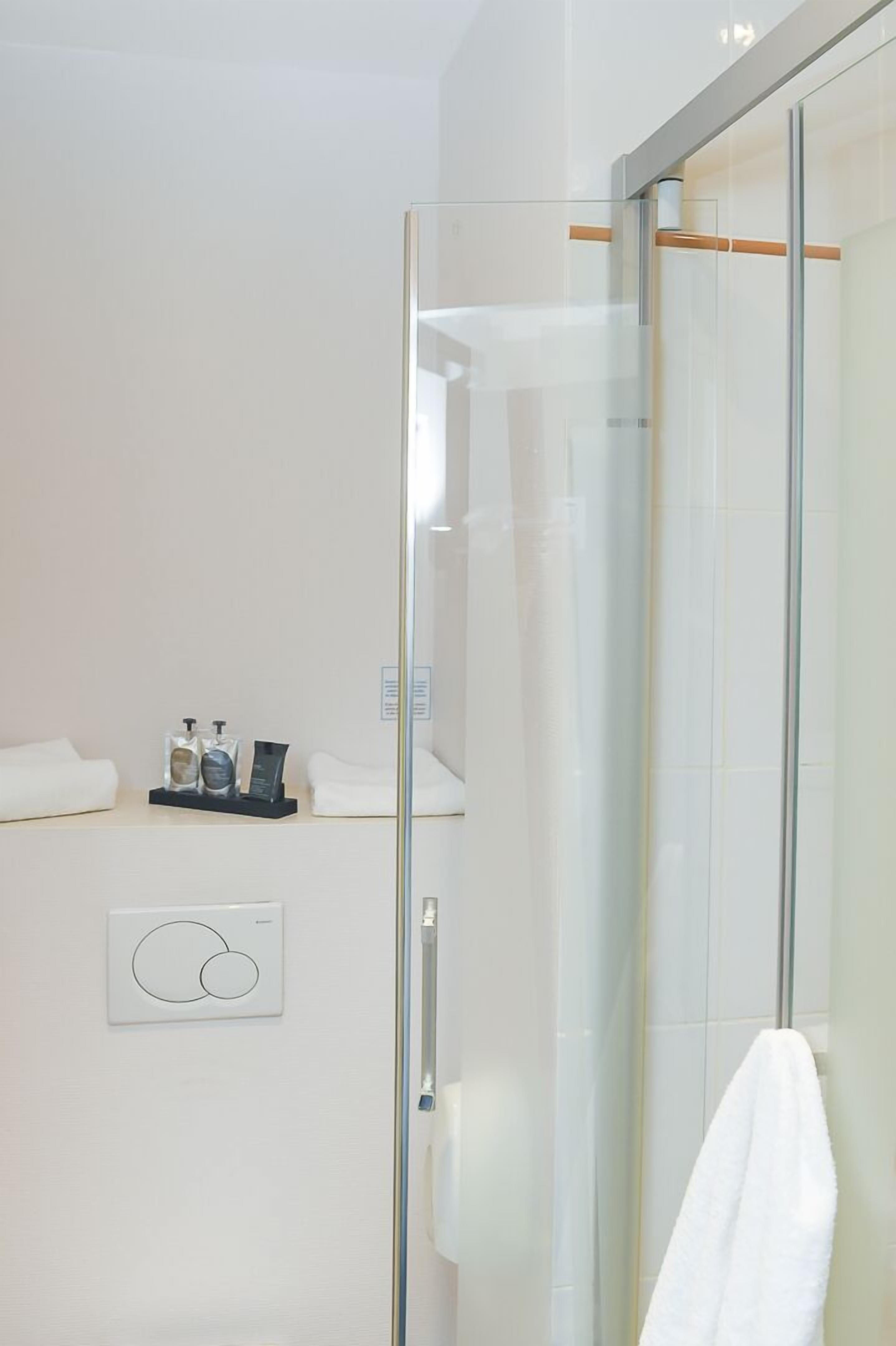 A modern bathroom with a glass shower enclosure, a white towel, and a small shelf with toiletries.