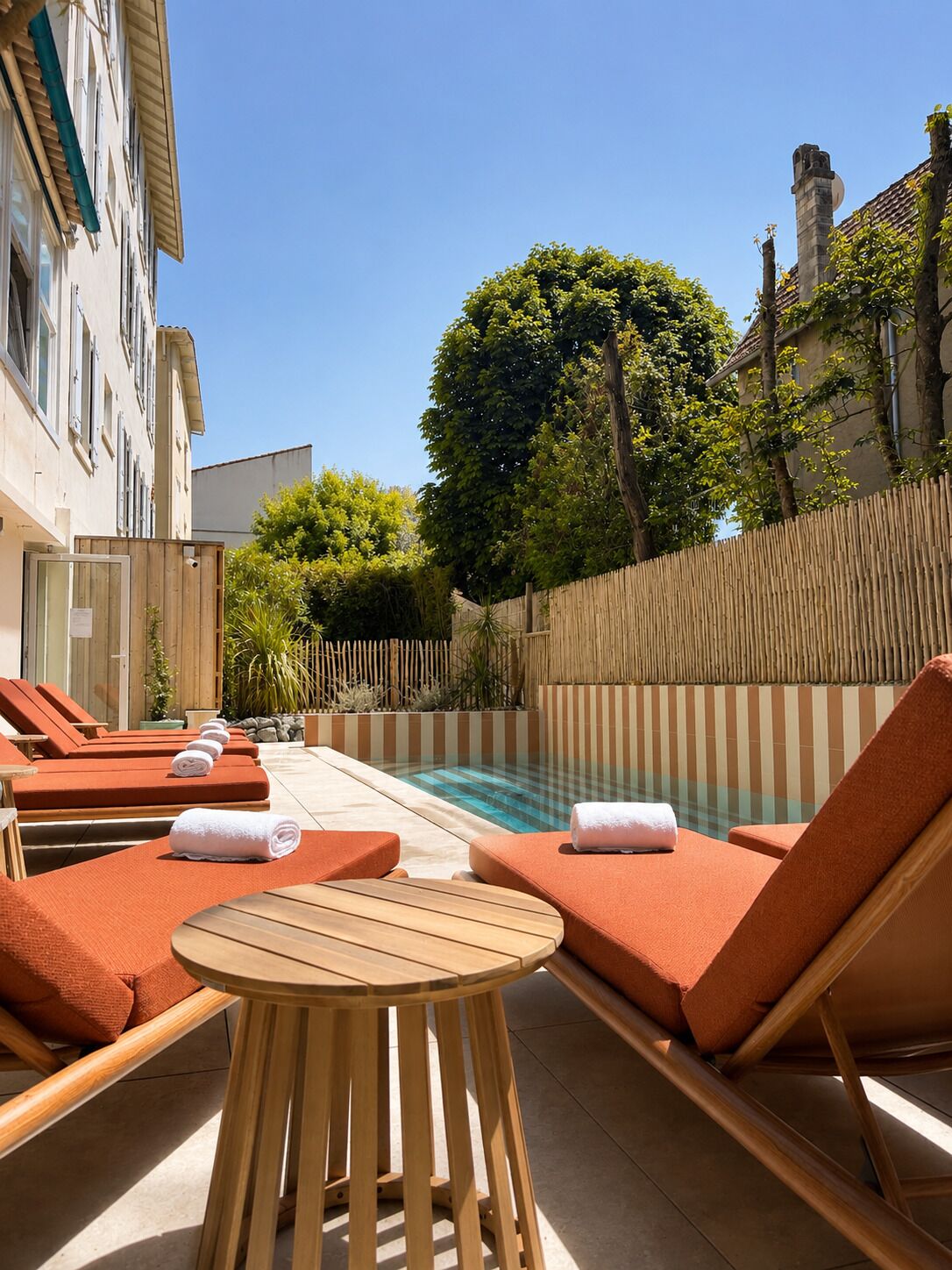 Un espace aménagé au bord de la piscine, avec des chaises longues, une petite table en bois et une piscine à l’eau d’un bleu limpide.