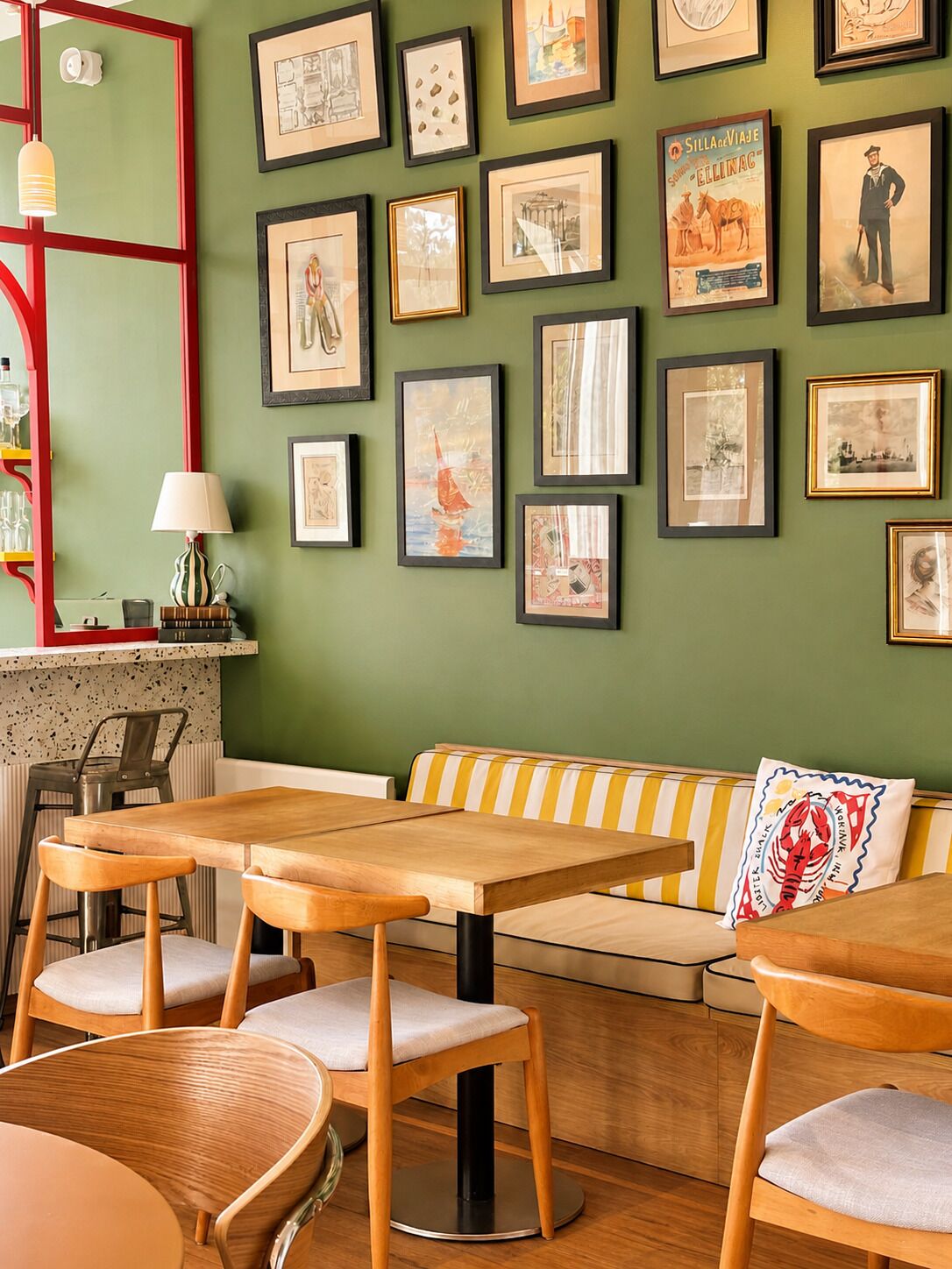 A cozy dining area with wooden tables and chairs, a striped bench, and a wall adorned with framed artwork.