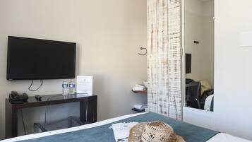 A hotel room with a bed, a desk with a telephone and a sign, a television, a mirror, and a bathroom with a shower curtain.