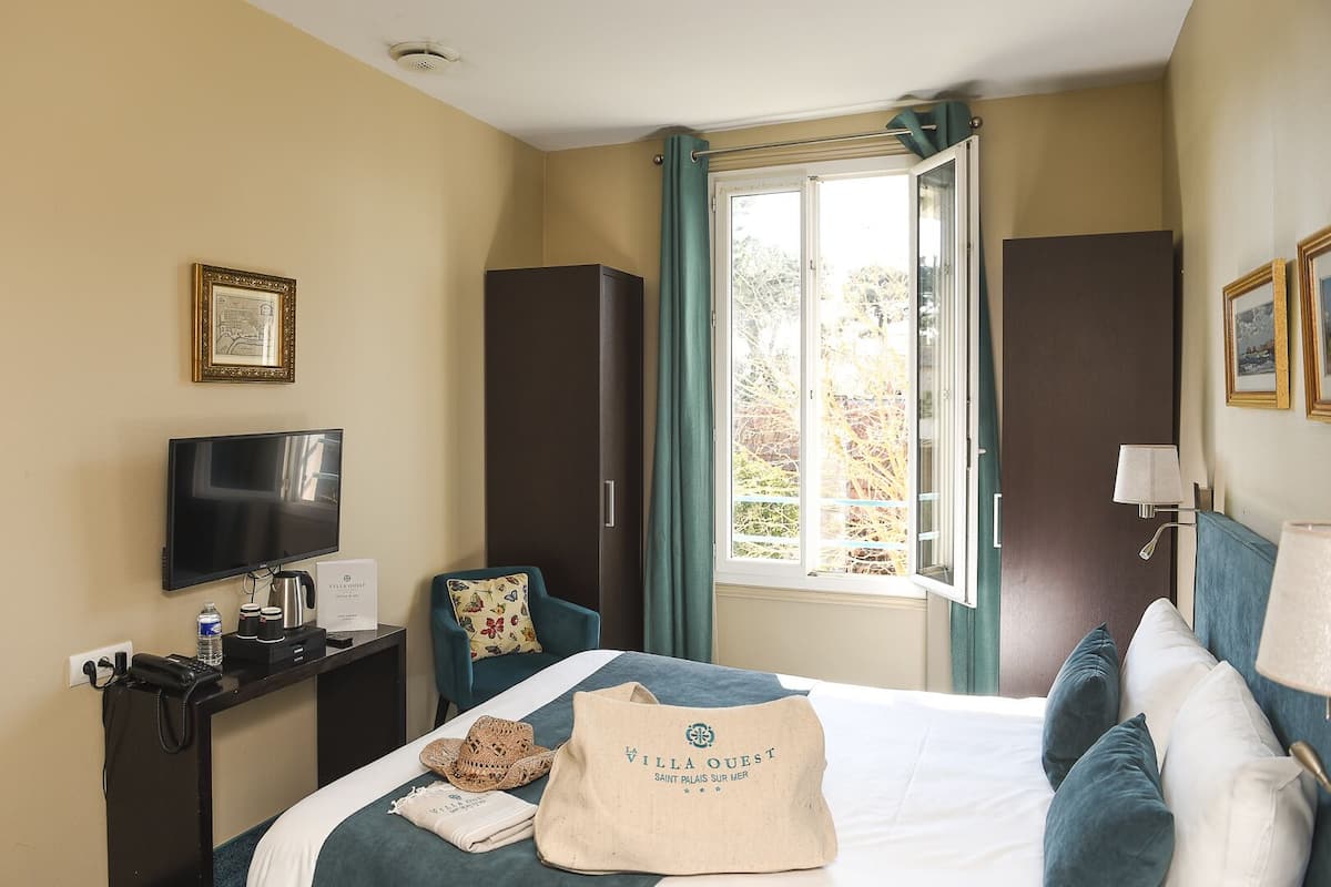Une chambre d’hôtel équipée d’un lit, d’une télévision, d’un bureau avec un téléphone, d’une chaise et d’une fenêtre avec des rideaux.