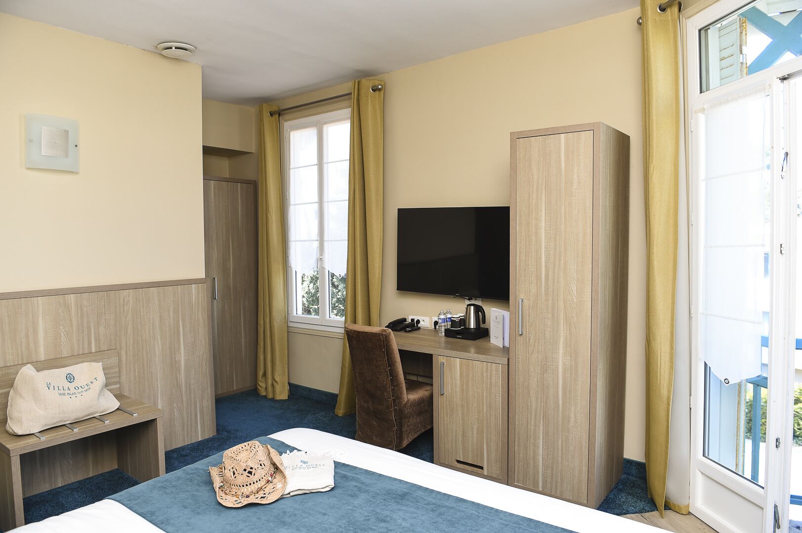 Een hotelkamer met een bed, een bureau met een televisie, een stoel en een raam met gordijnen.