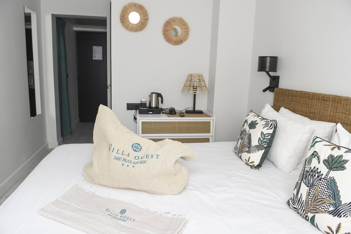 Une chambre d’hôtel comprenant un lit, des oreillers, une table de chevet, une lampe et un mur orné de deux miroirs décoratifs.