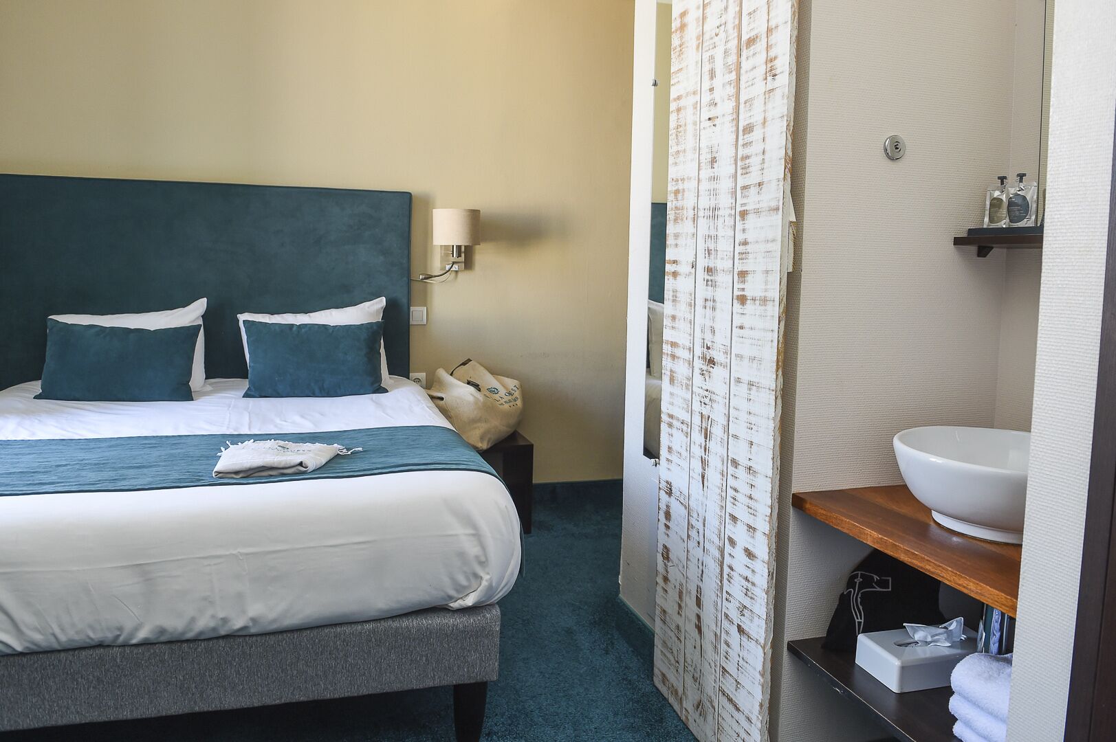 A hotel room with a bed, a bedside table, a bathroom with a sink and mirror, and a shower curtain.