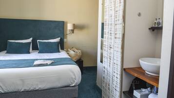 A hotel room with a bed, a bedside table, a bathroom with a sink and mirror, and a shower curtain.