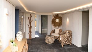 Un intérieur moderne avec un plafond incurvé, un coin salon avec un fauteuil en osier et une petite table, ainsi qu’un élément décoratif mural.