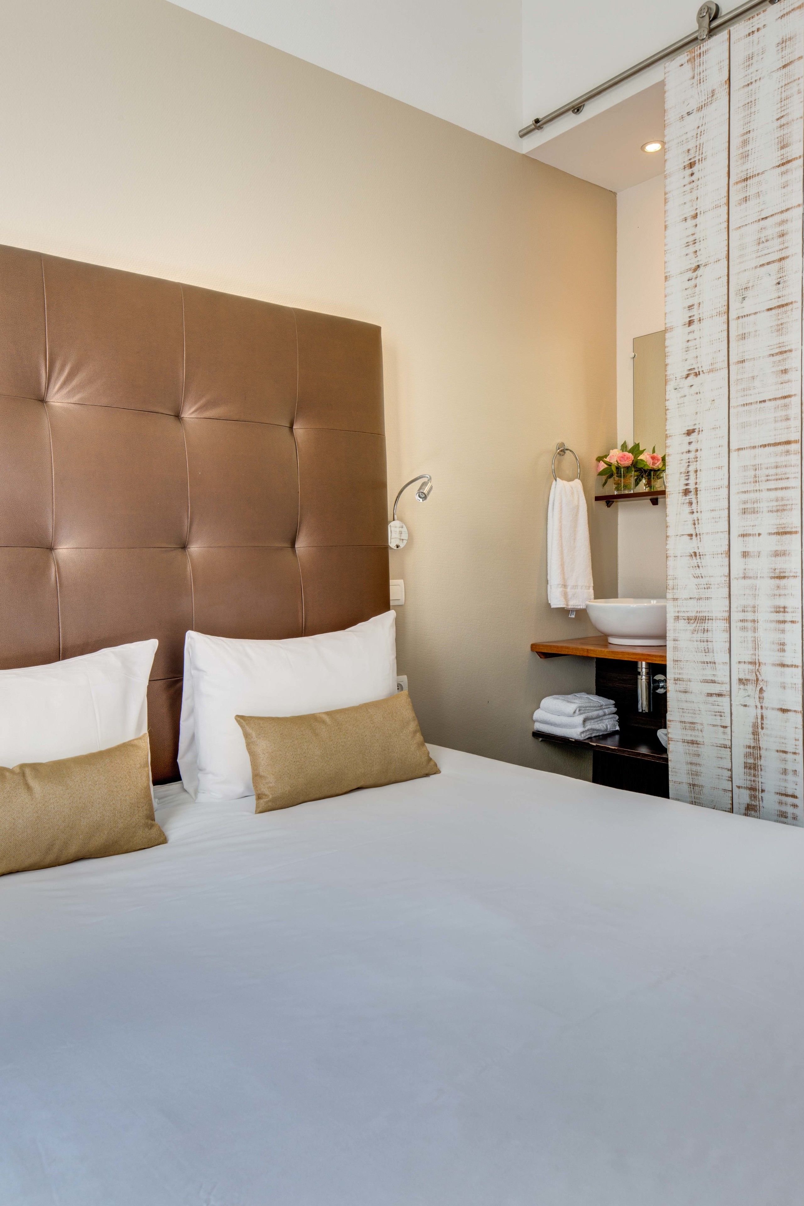 Una habitación de hotel con una cama grande, cabecera, mesita de noche, lavabo blanco y un espejo.