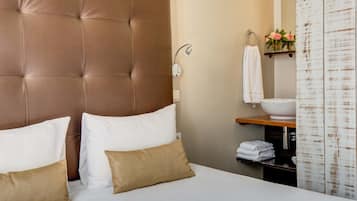 Una habitación de hotel con una cama grande, cabecera, mesita de noche, lavabo blanco y un espejo.