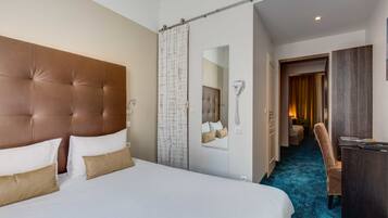 Quarto de hotel com uma cama grande, uma escrivaninha, uma cadeira e um banheiro visível através de uma porta aberta.