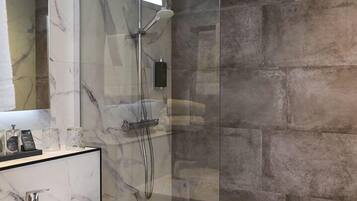 Un baño moderno con ducha de vidrio, pared de azulejos de mármol y tocador de madera con lavamanos.