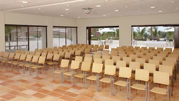A conference room with rows of chairs, large windows, and a view of palm trees.