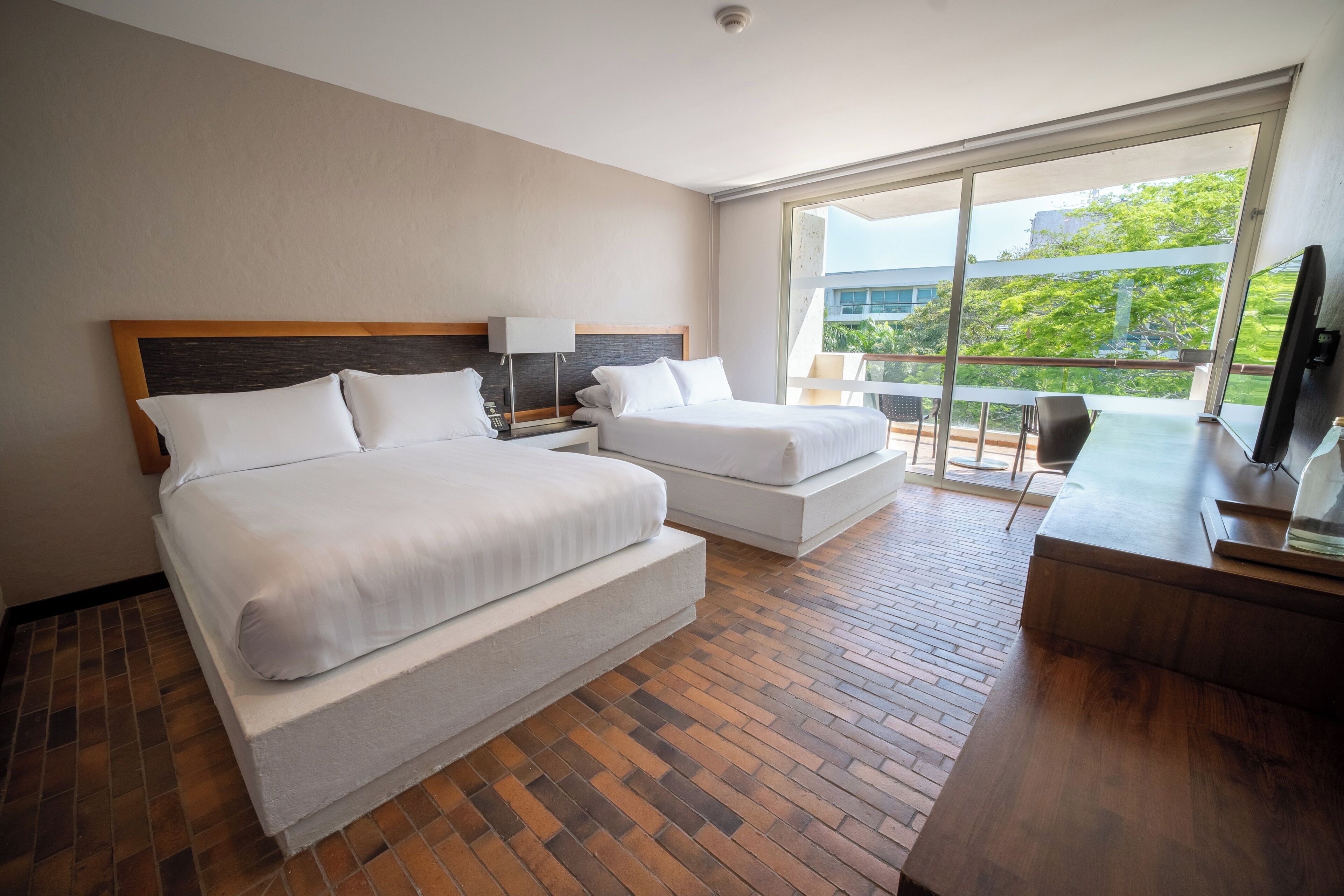 A hotel room with two beds, a desk, a chair, and a balcony with a view.