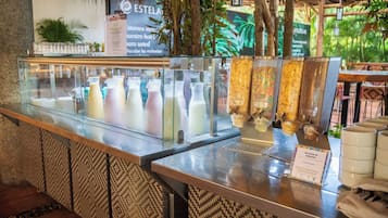Una barra de desayuno con un expositor de vidrio que contiene diversas bebidas y un cartel con el menú.