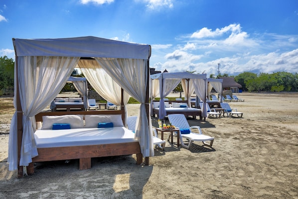 A beach resort with canopy beds and lounge chairs.