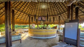 An outdoor bar area with a thatched roof, round bar counter, and seating arrangements. - Hotel Estelar Playa Manzanillo (Cartagena)