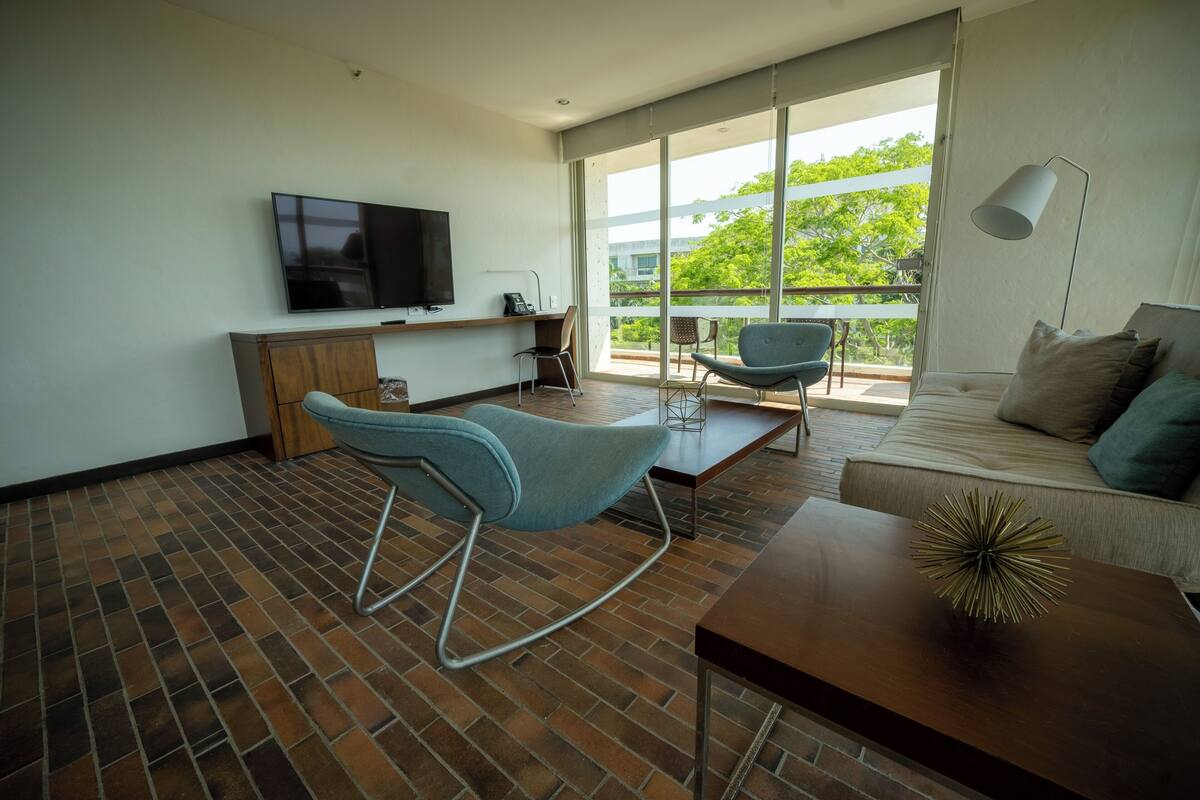 Ein modernes Wohnzimmer mit Fernseher, einer Couch, Sesseln und einem Balkon mit Blick.