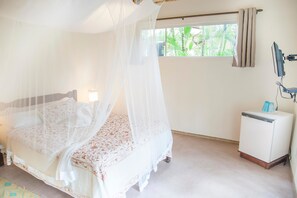 A bedroom with a four-poster bed, a small bedside table, a television, and a window with curtains. - Pousada Peki (Arraial d'Ajuda)