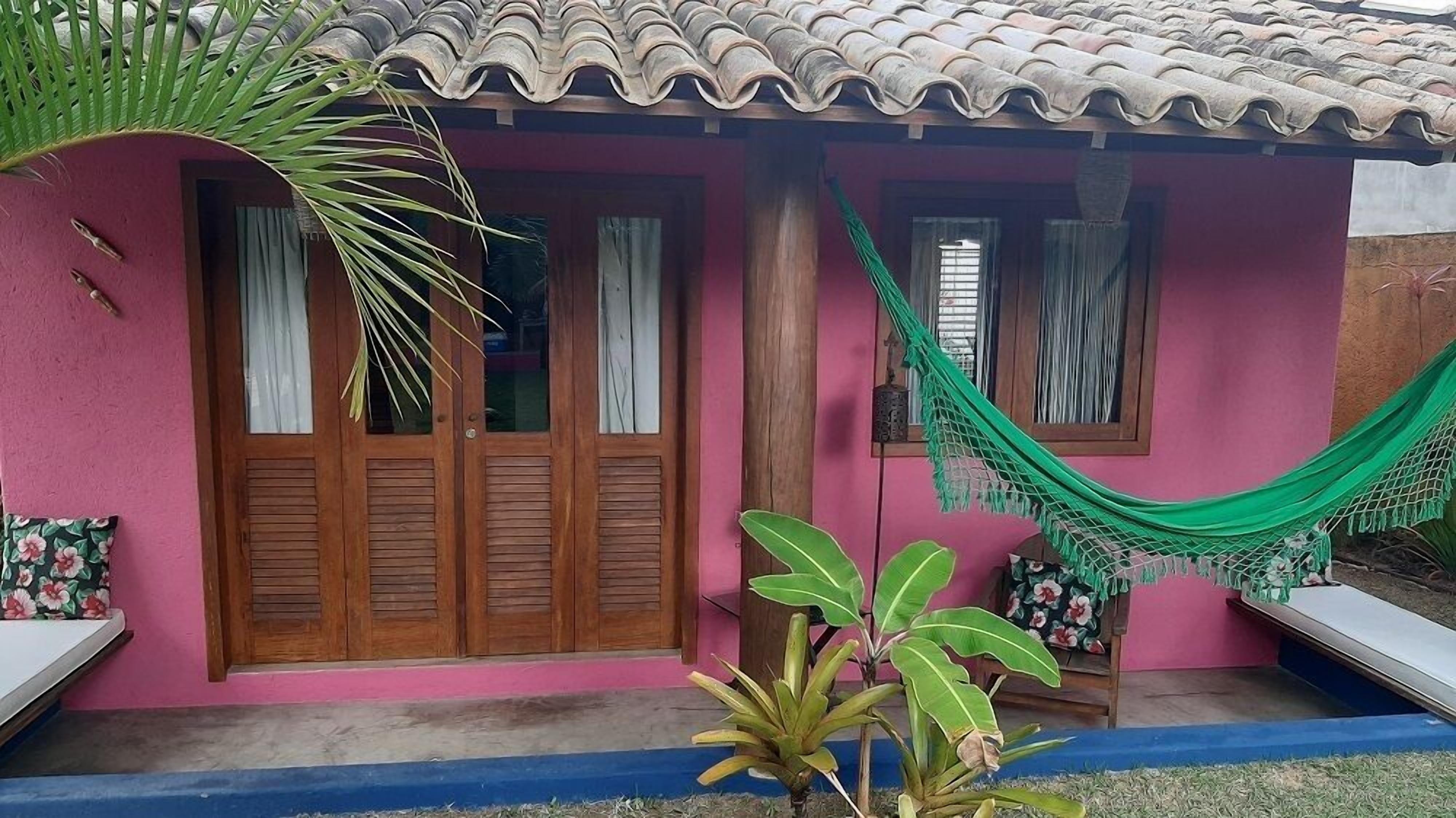 A house with a pink facade, wooden doors, and a green hammock.
