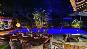 An outdoor dining area with a pool, wicker chairs, and a wooden deck. - Guest House Villa 2 Santos (Porto Seguro)