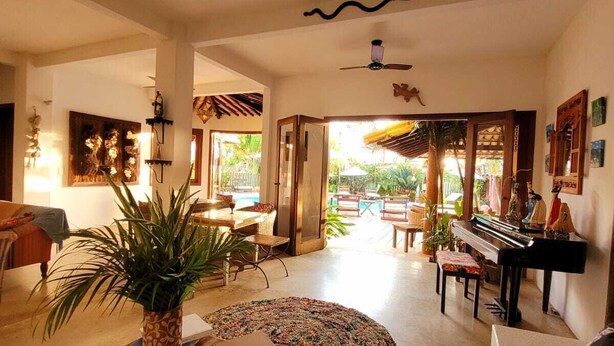 A spacious living area with a piano, a coffee table with books, and a large plant. - Guest House Villa 2 Santos (Porto Seguro)