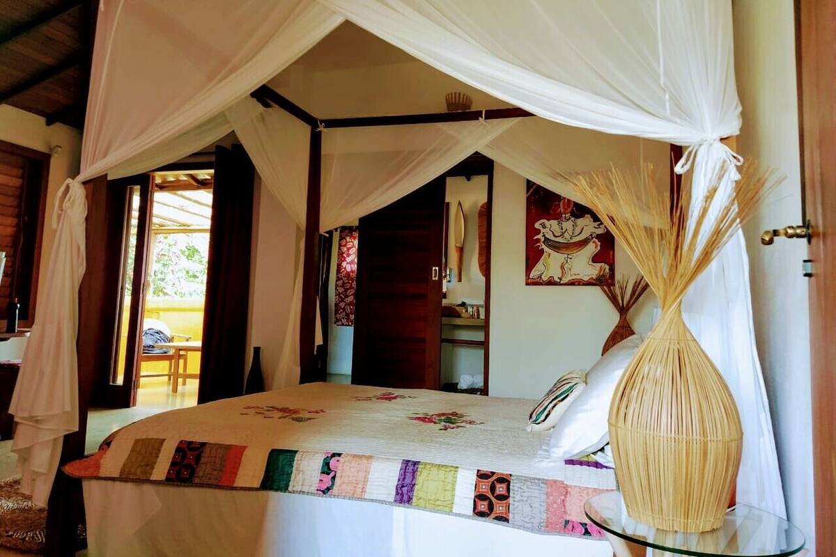 A bedroom with a canopy bed, a wooden door, and a vase on a table.