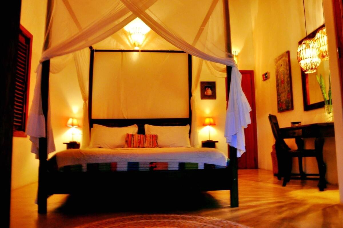 A four-poster bed with white linens, two bedside lamps, and a canopy.