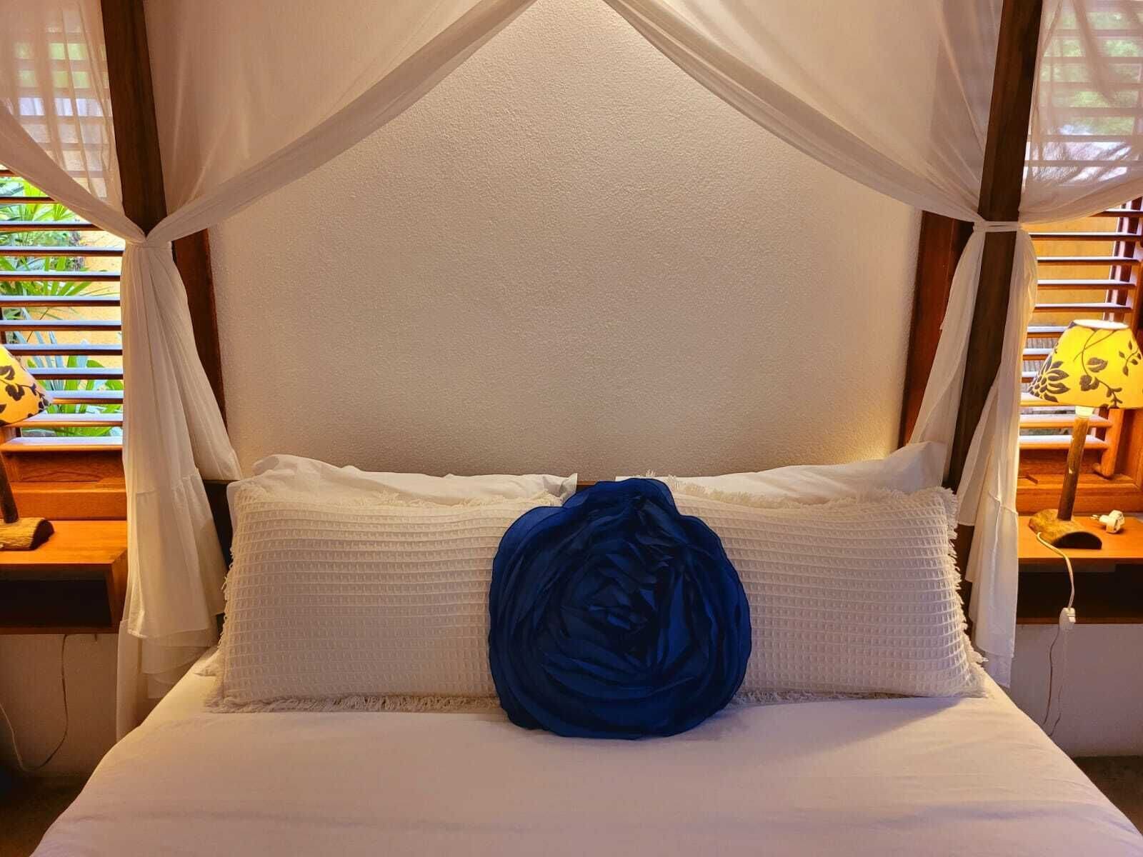 A bed with a canopy, white bedding, and a blue decorative pillow.